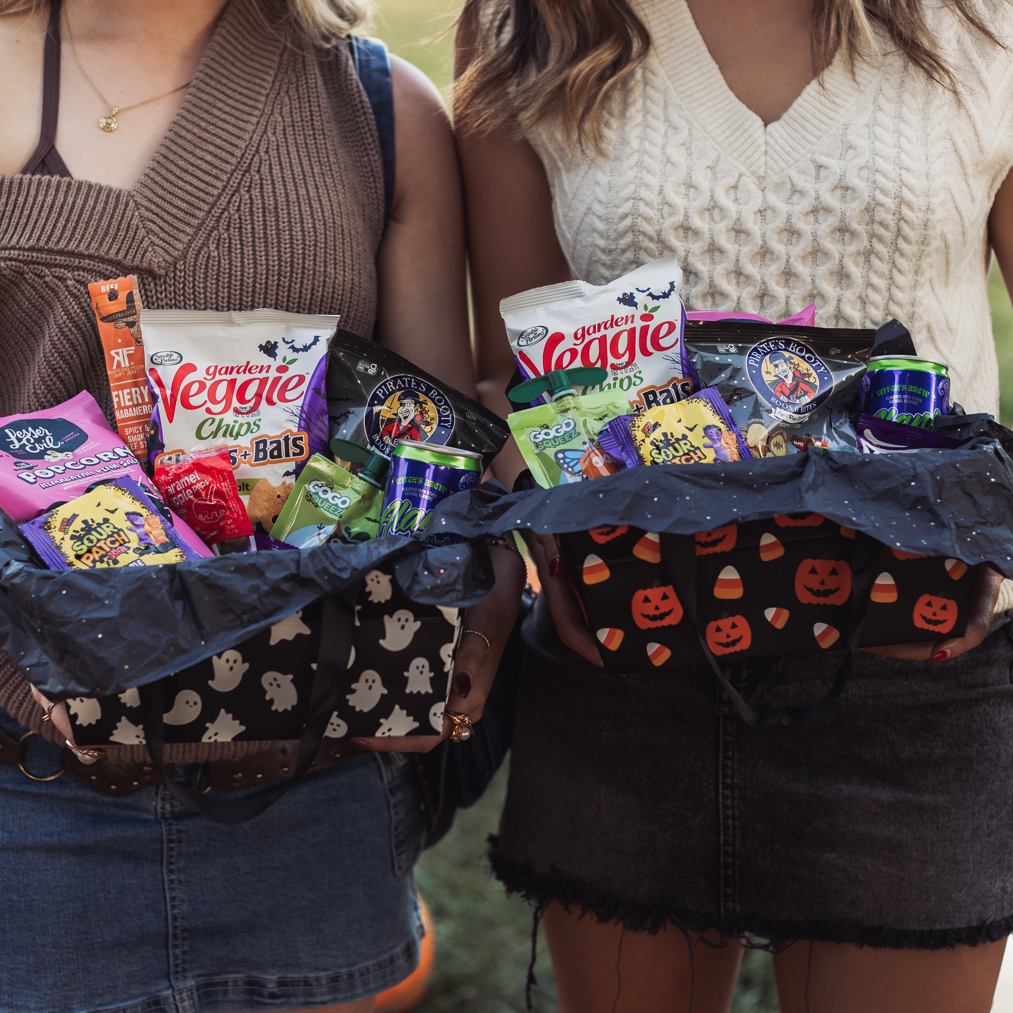 Two friends holding Glutique Halloween Boo Boxes filled with gluten-free snacks, candy, and drinks in festive pumpkin and ghost packaging.